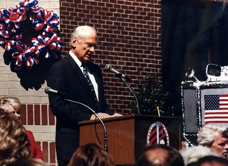 Photograph of Buzz Aldrin standing at a podium delivering his remarks at Aldrin Elementary School’s dedication ceremony. 