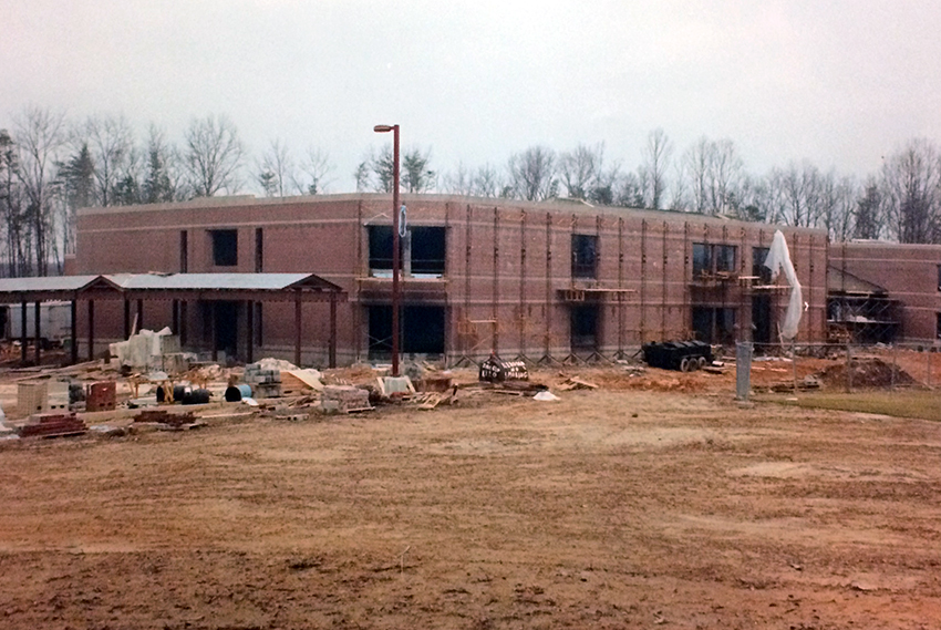 Photograph of the rear of Aldrin Elementary School taken from the south. The brick veneer is in place on all visible sides of the building. Scaffolding is in place along sections of the exterior where work is being done on the windows. Construction supplies and materials are on the ground close to the building. 