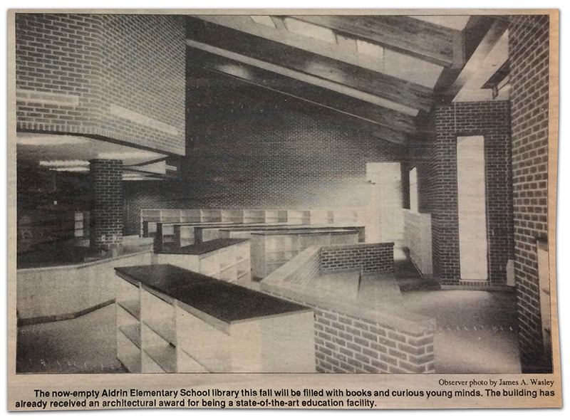 Newspaper clipping from the Reston Observer, published on April 14, 1994. A black and white photograph shows the interior of the library. The bookshelves are empty and the walls are unadorned. The photograph caption states: The now-empty Aldrin Elementary School library this fall will be filled with books and curious young minds. The building has already received an architectural ward for being a state-of-the-art education facility. 