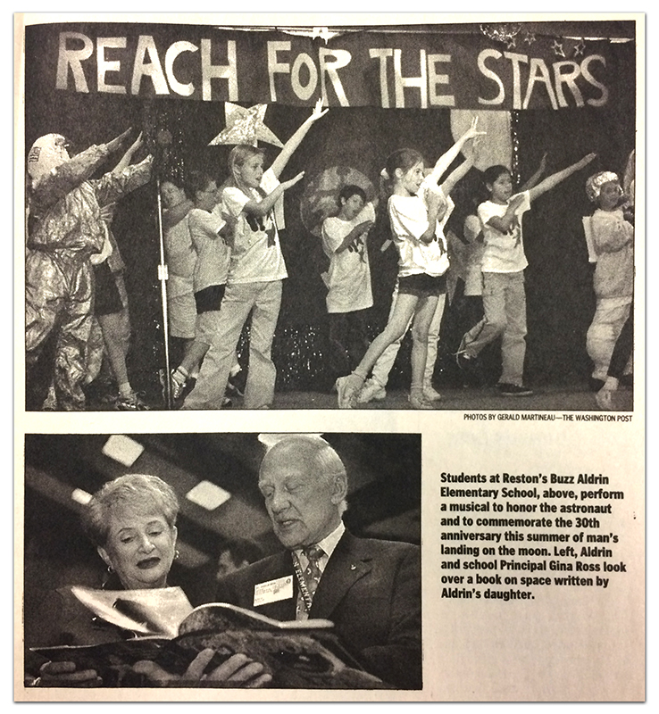 Newspaper clipping from a Washington Post article about the anniversary commemoration. Two photographs are shown, both in black and white. At top, students are performing a musical. The children are standing on a stage, singing in unison, with their arms raised in the air. A banner with the words Reach for the Stars is affixed to a black curtain behind them. Beneath this picture is a photograph of Principal Gina Ross standing with Buzz Aldrin. They are looking through a book that Aldrin is holding. The photograph caption reads: Students at Reston's Buzz Aldrin Elementary School, above, perform a musical to honor the astronaut and to commemorate the 30th anniversary of man's landing on the moon. Left, Aldrin and school Principal Gina Ross look over a book on space written by Aldrin's daughter. 